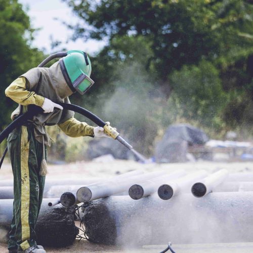 Male worker sandblasting dust process cleaning pipeline surface on steel before painting in the factory.