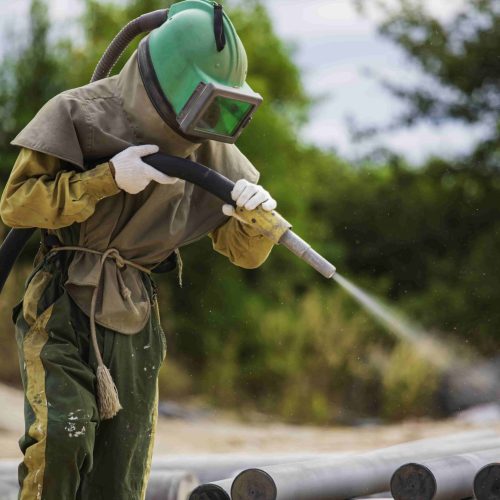 Male worker Sand blasting process cleaning pipeline surface on steel before painting in factory.